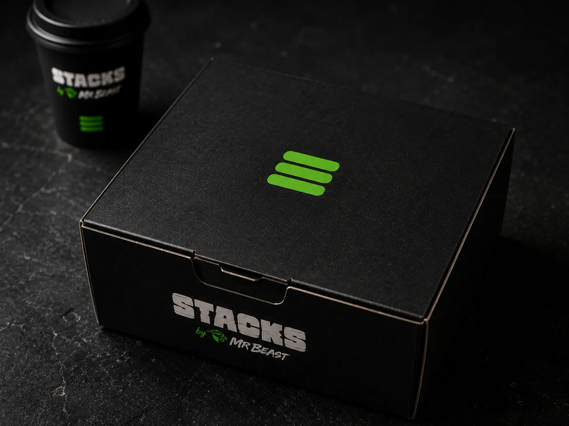 Stacks black takeout box and coffee cup on a dark counter with green stack mark